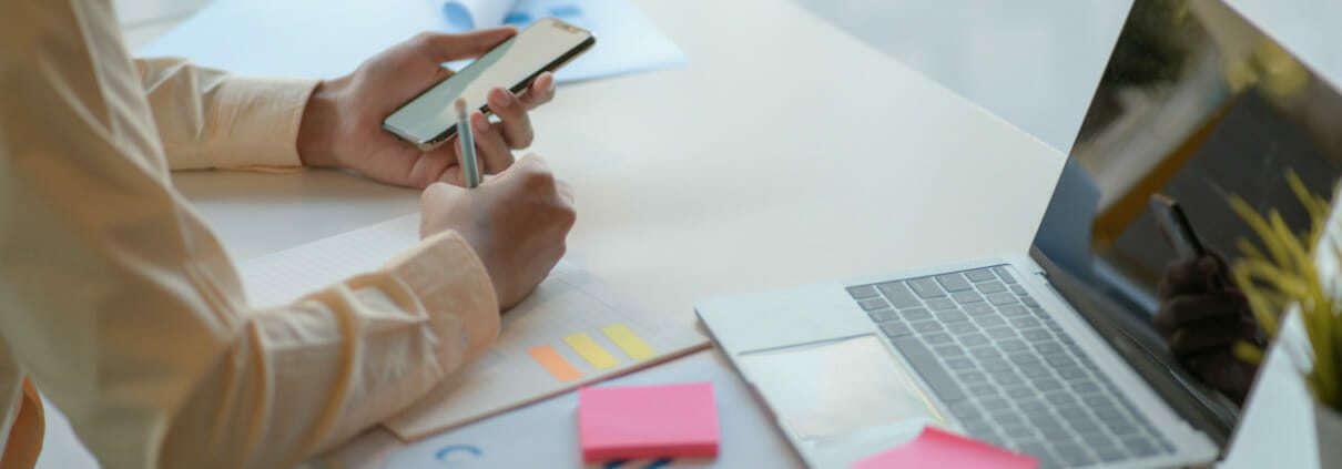 Office man taking notes and using a smartphone on a desk with a laptop.